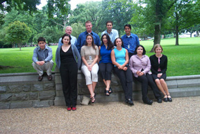 A group of eleven Bingaman inters, five men and six women, sitting on a stone wall adjacent to the grassy expanse opposite the capitol.