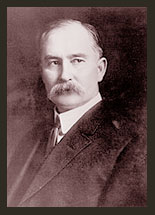 A black and white photo of Senator Albert B. Fall, who wears a dark suit, white shirt, and tie, and has a heavy moustache.