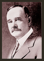 A black and white photo of Senator Andriues A. Jones, who wears a light grey jacket, a white shirt, and a tie. Senator Jones has a moustache and is looking toward the camera.