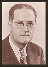 Black and white photograph of Senator Clinton P. Anderson, who is wearing a dark jacket, a white shirt, and striped tie. Senator Anderson wears eyeglasses.