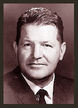 A black and white photo of Senator Edwin L. Mechen, who is facing the camera and smiling. Senator Mechem is wearing a darkish jacket, white shirt, and striped tie.