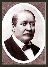 A black and white photo of Senator Thomas B. Catron, who wears a dark suit, white tie, and bowtie, and has a heavy moustache.