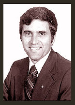 Black and white photo of Senator Harrison H. Schmitt. Senator Schmitt is wearing a black jacket, black tie, and white shirt.