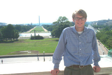 Photo of intern Carson Smith, who is resting against a marble ledge outside the Capitol. In the distance behind him is the National Mall and the Washington Monument.