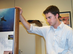 Photo of intern Hugh Naylor, who had his hand on the edge of a partition and is looking downward at something not visible in the photo.