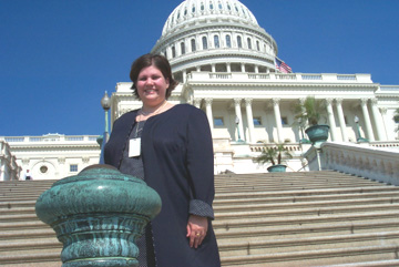 A photo of intern Anna Marie Baca, who stands beside a bannister outside the Capitol, with a lon line of steps behind her leading up to the Capitol dome