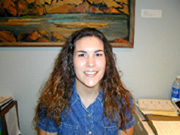 A graphic of a young woman intern sitting at a desk. She is smiling into the camera. Behind her is a wall painting of a southwestern scene.