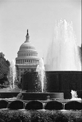 The U.S. Capitol Dome as seen from one of the many parks on Capital Hill. A water fountain in the foreground sprays water high into the air. Because of the perspective, the water appears to reach the height of the Capitol dome in the background.